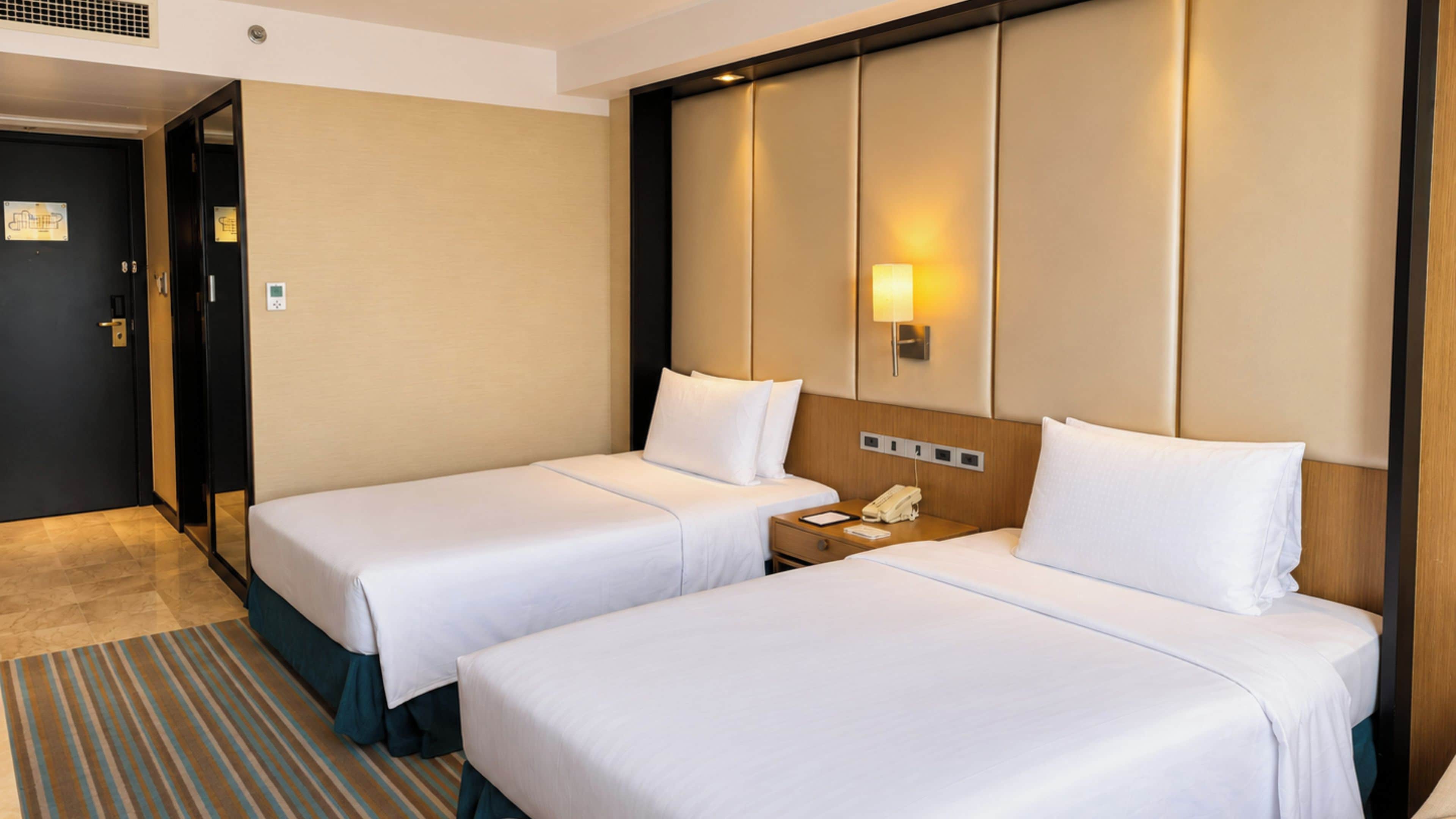 Una habitación de hotel con dos camas, una mesita de noche con teléfono y una lámpara fijada a la pared.