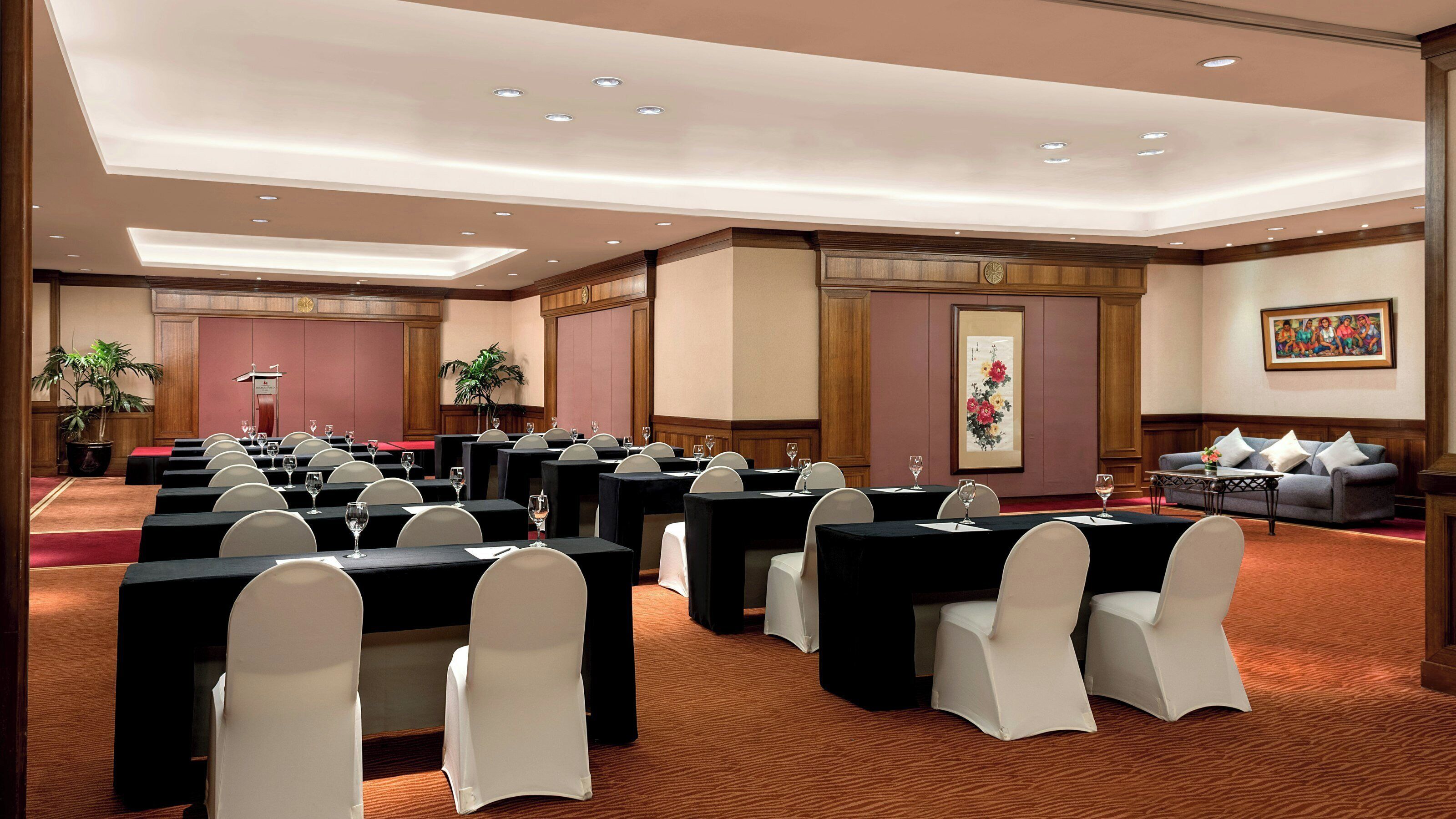 A conference room with multiple tables and chairs, a podium, and a painting on the wall.