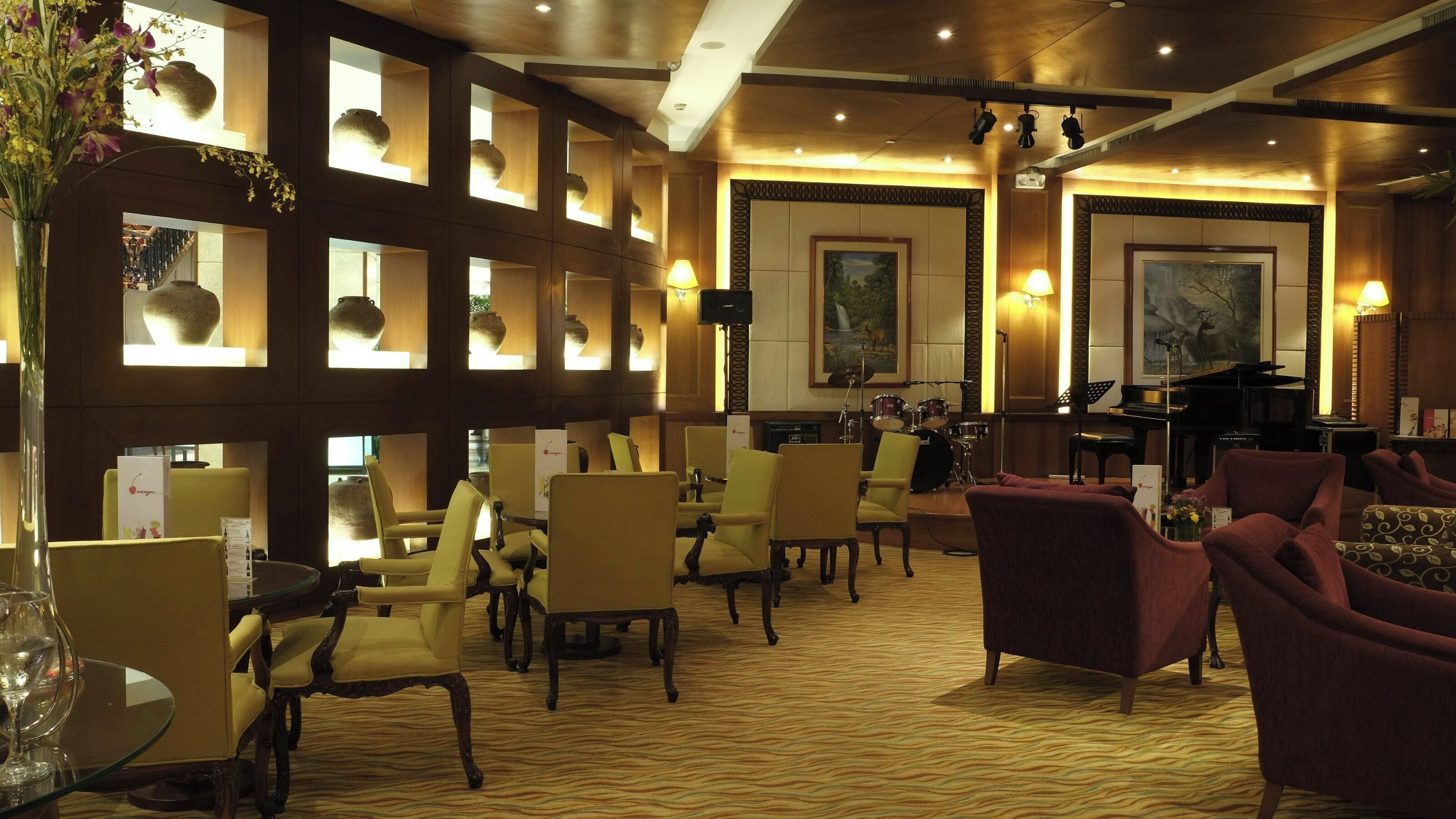 A hotel lobby with multiple seating areas, a piano, and a stage with musical instruments.