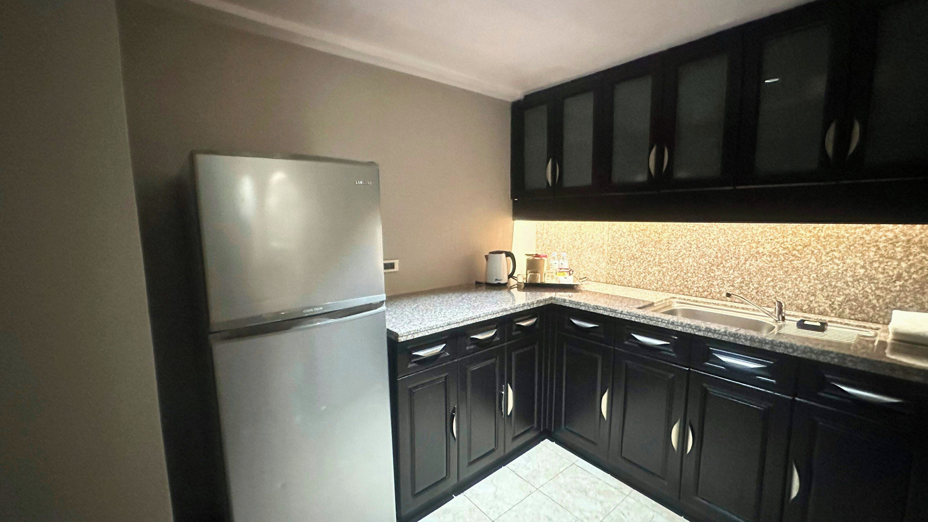 A kitchen with a refrigerator, dark cabinets, a countertop, and a sink.