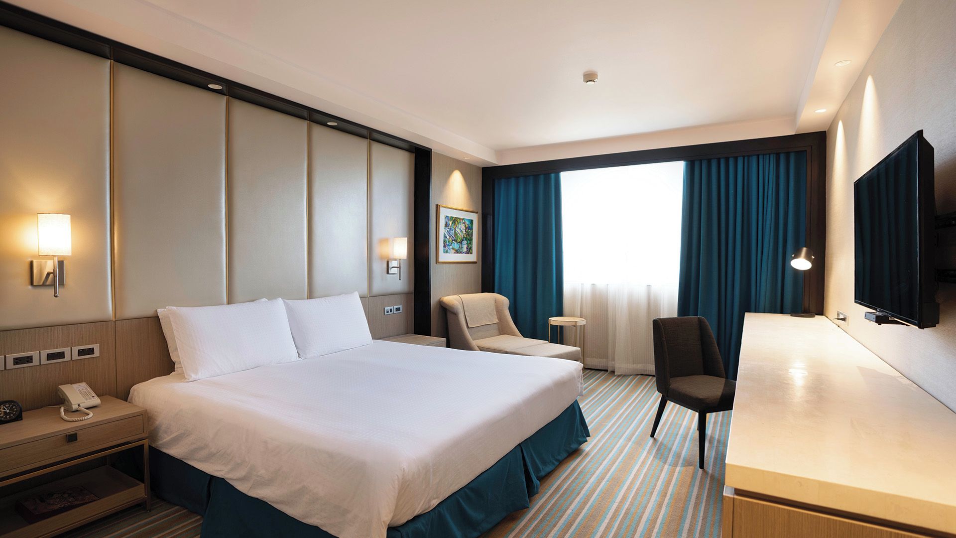 A hotel room with a large bed, a desk, a chair, a telephone, and a TV.