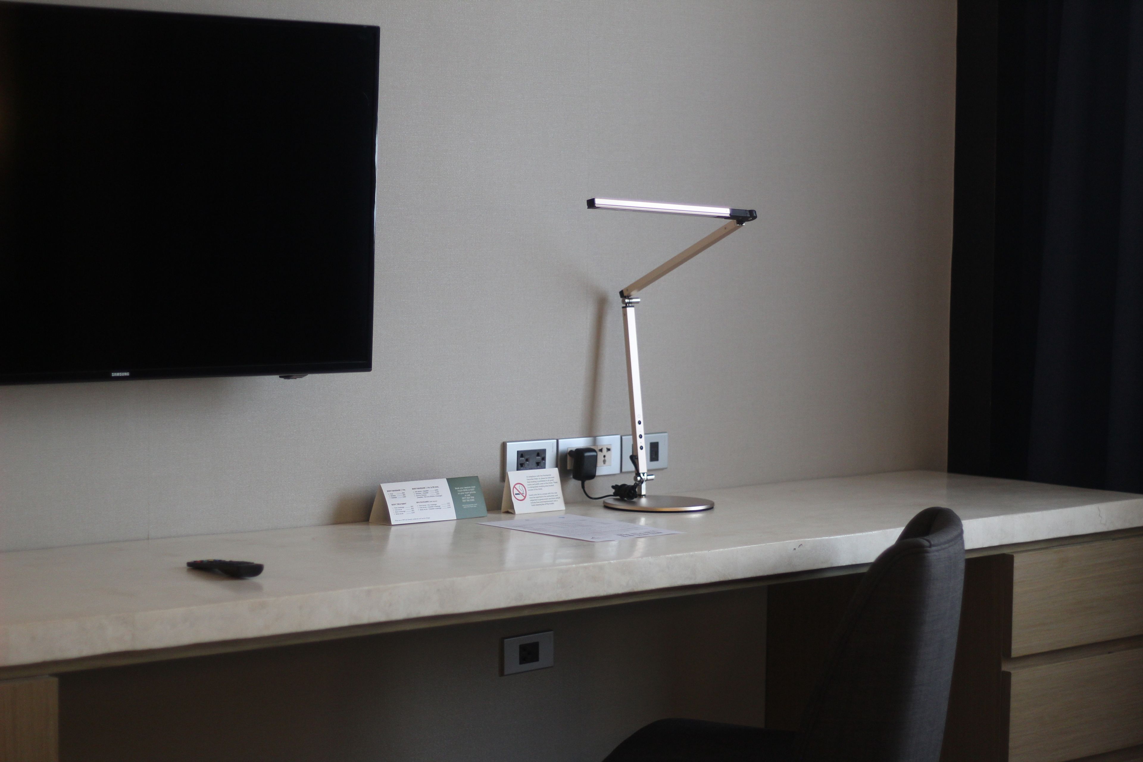 A hotel desk with a flat-screen TV, a desk lamp, a phone, and a notepad.