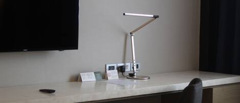 A hotel desk with a flat-screen TV, a desk lamp, a phone, and a notepad.