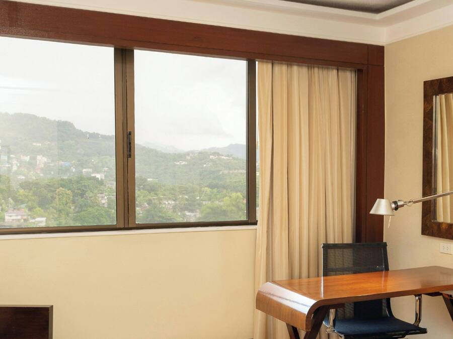A hotel room with a large window, a desk, a chair, and a mirror.