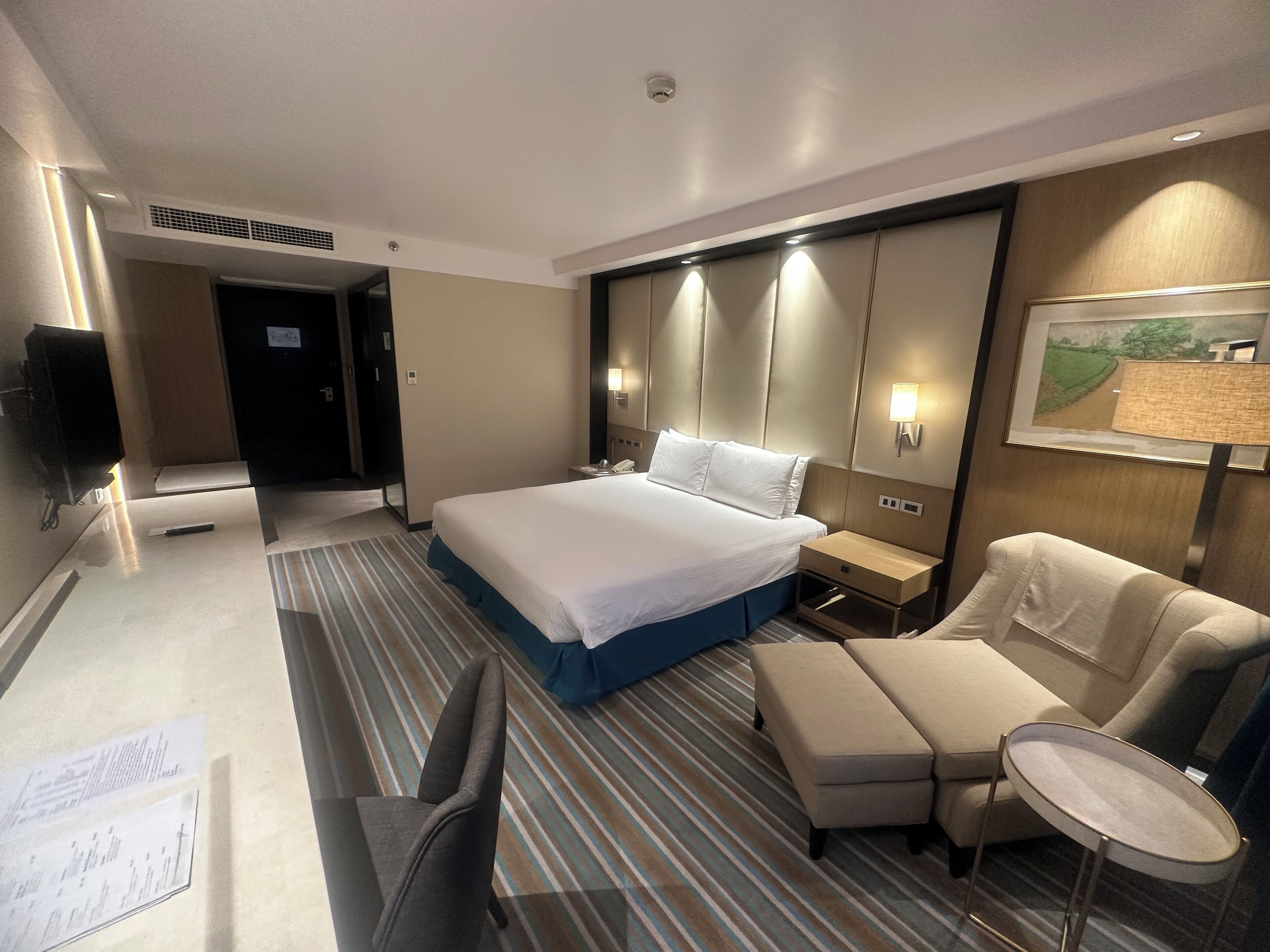 A hotel room with a large bed, a desk with a chair, a small table, and a sofa.