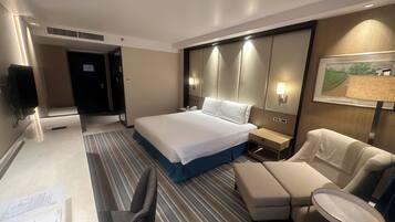 A hotel room with a large bed, a desk with a chair, a small table, and a sofa.