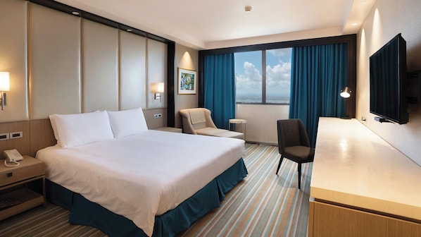 Habitación de hotel con una cama grande, un escritorio, una silla, un televisor y una ventana con cortinas.