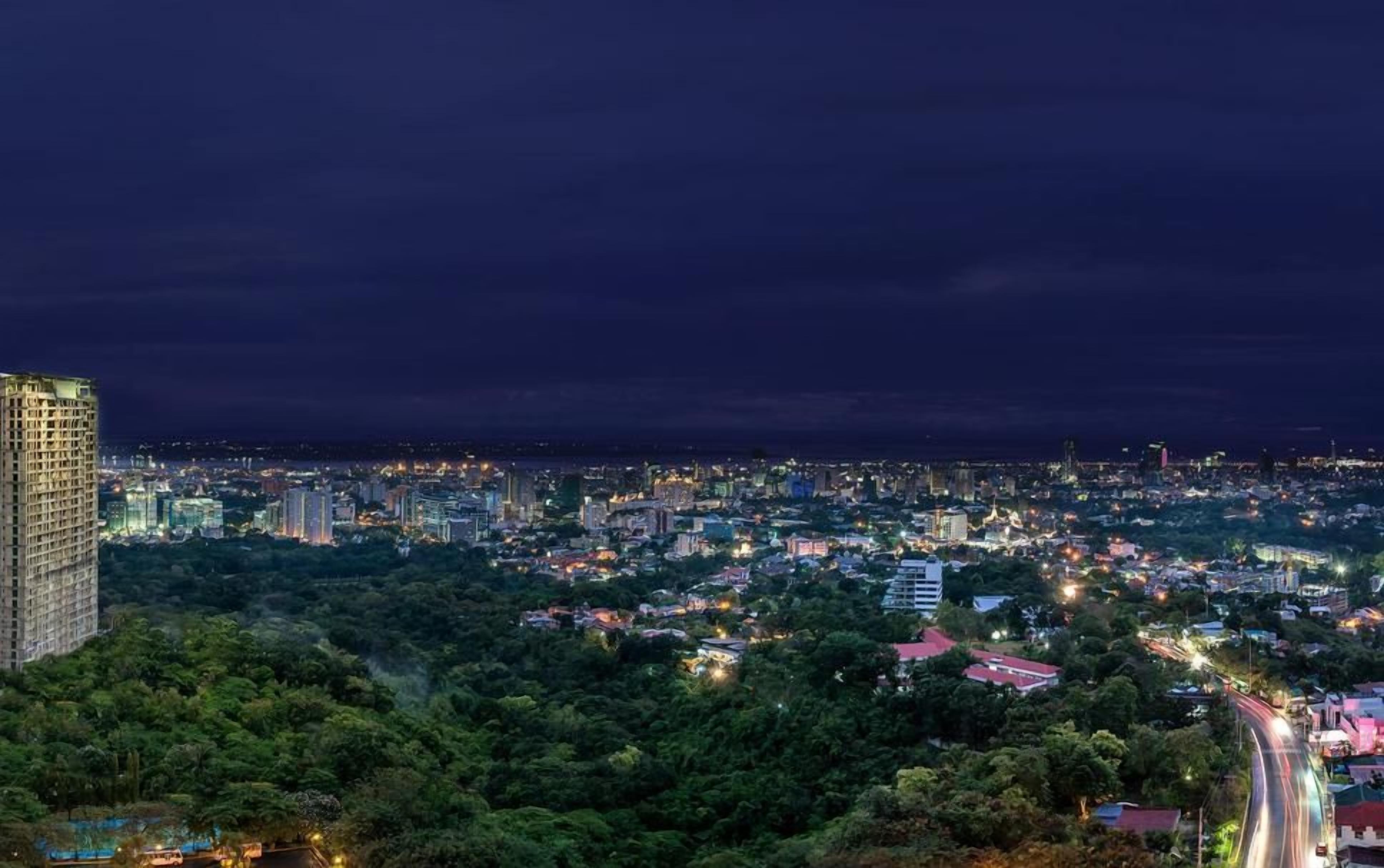 A cityscape at night with a prominent high-rise building on the left and a dense urban area with illuminated streets.