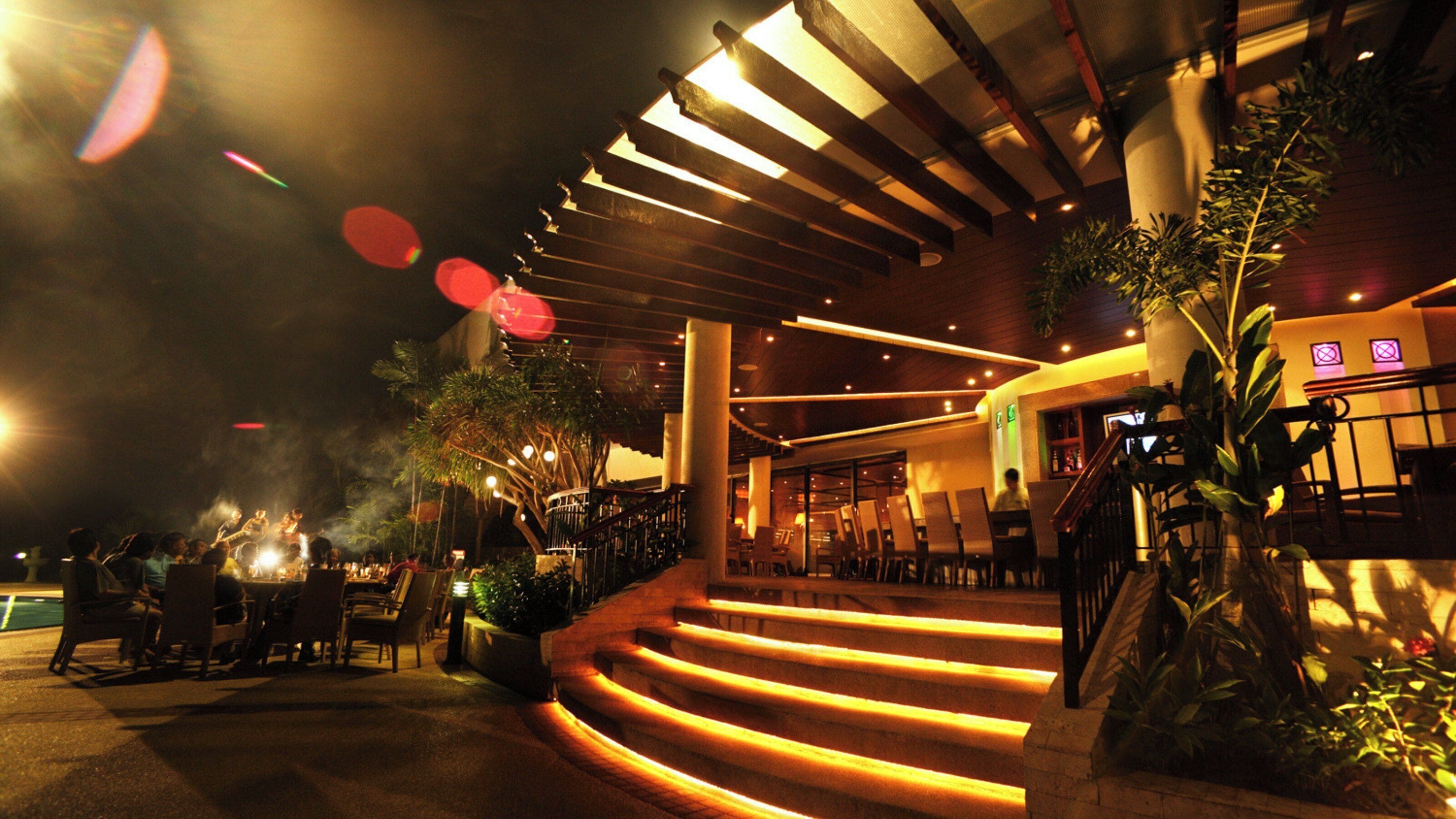 A modern building with a staircase leading to an upper level, indoor plants, and a bar area.