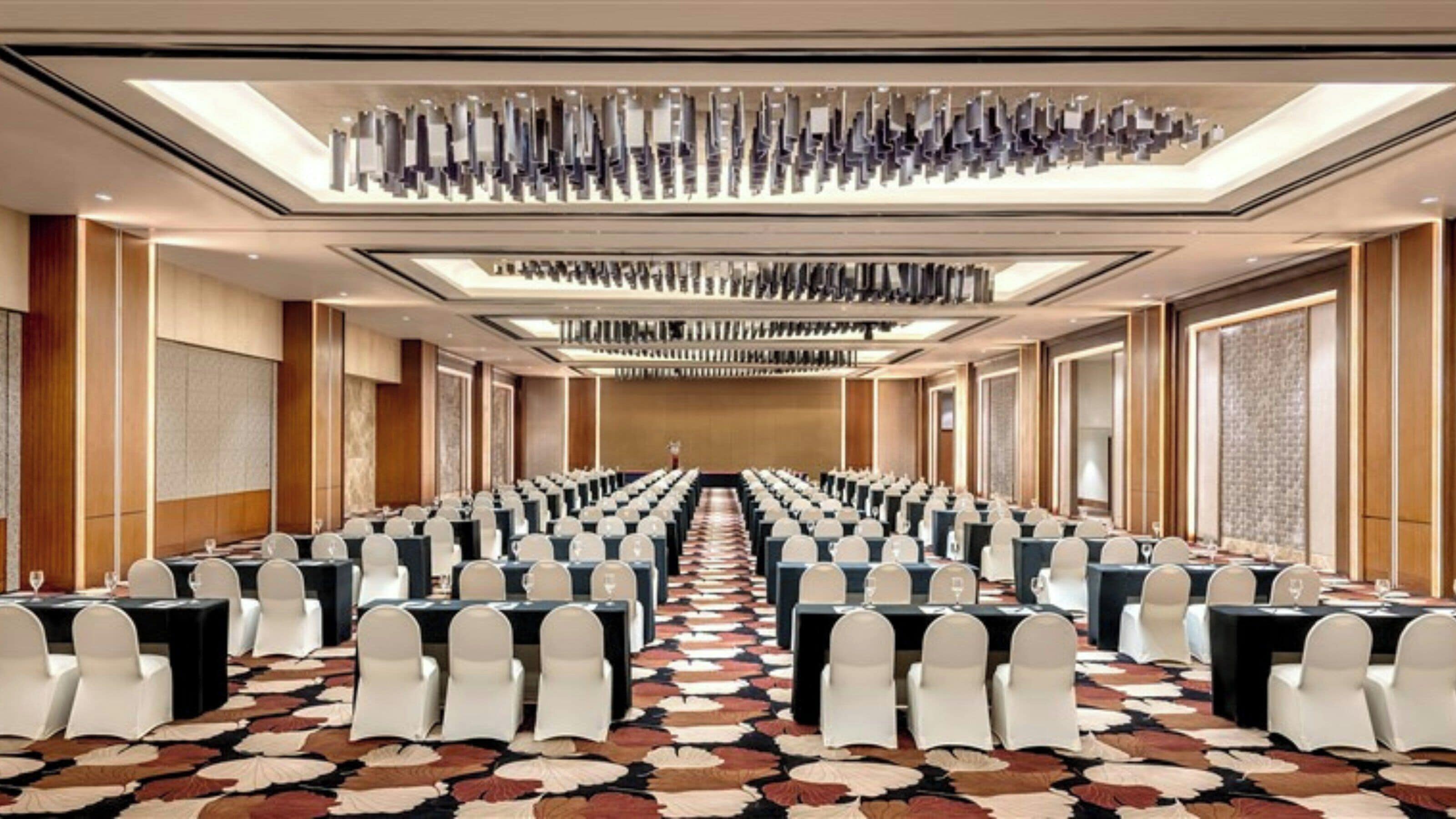 A conference room with rows of tables and chairs, a patterned carpet, and a modern ceiling design.