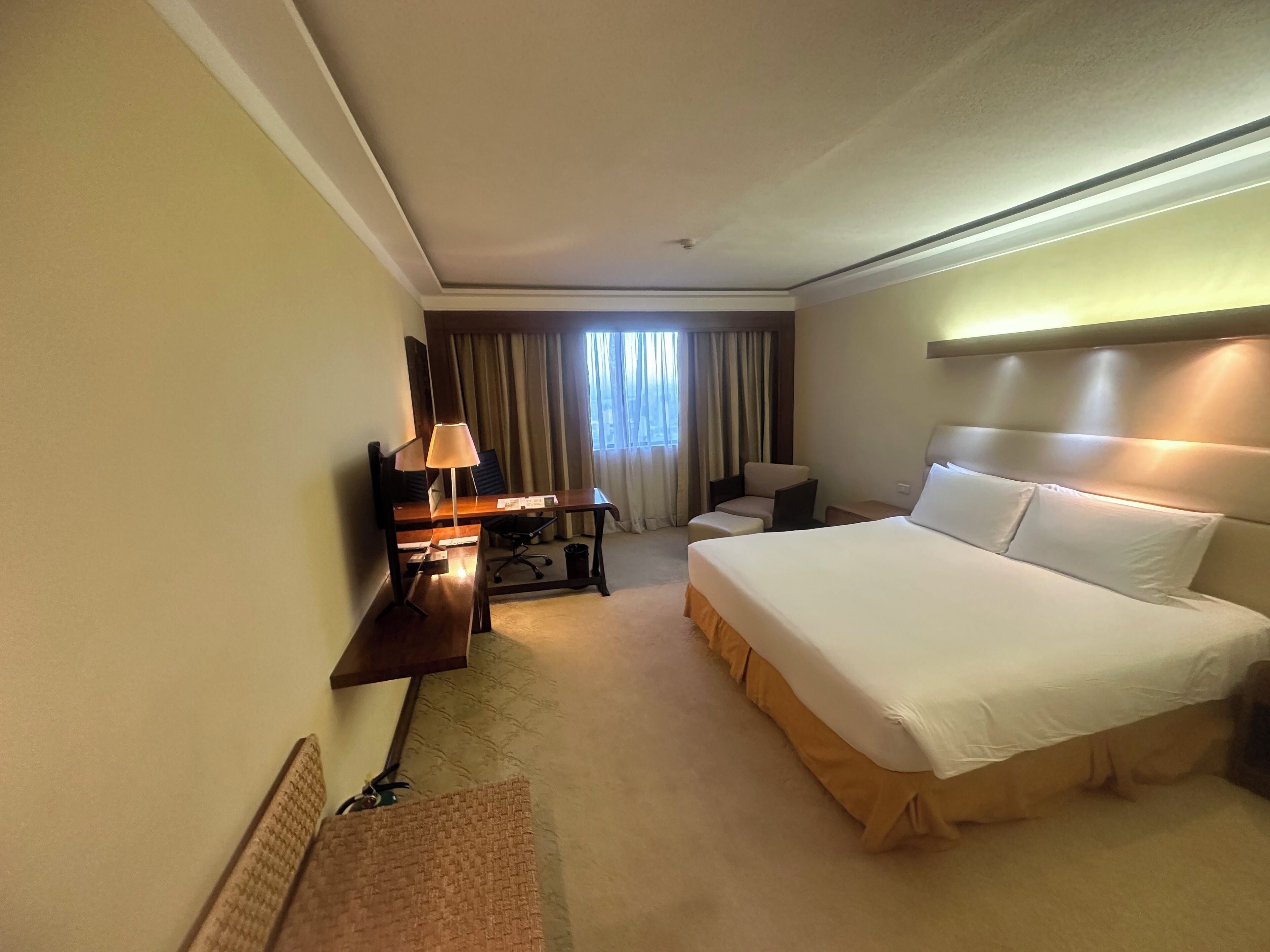 Een hotelkamer met een groot bed, een bureau met een lamp, een stoel en een klein tafeltje.