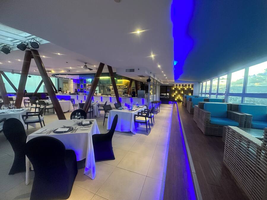 A restaurant with tables and chairs, a bar area, and a view through large windows.