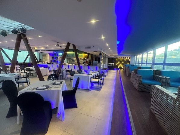 A restaurant with tables and chairs, a bar area, and a view through large windows. - Marco Polo Plaza Cebu (Cebu City)