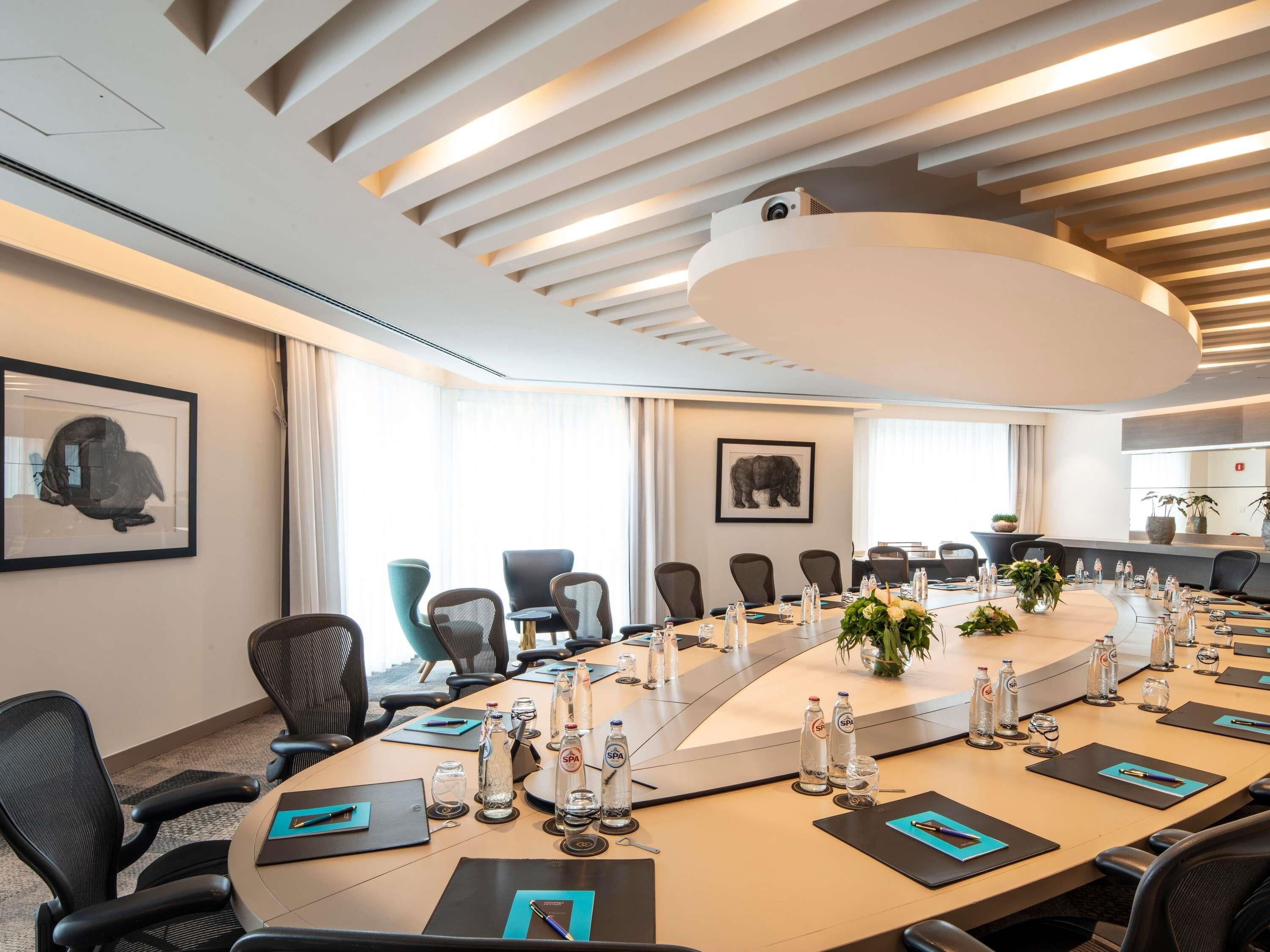 A modern conference room with a long table, chairs, water bottles, and framed artwork on the walls.
