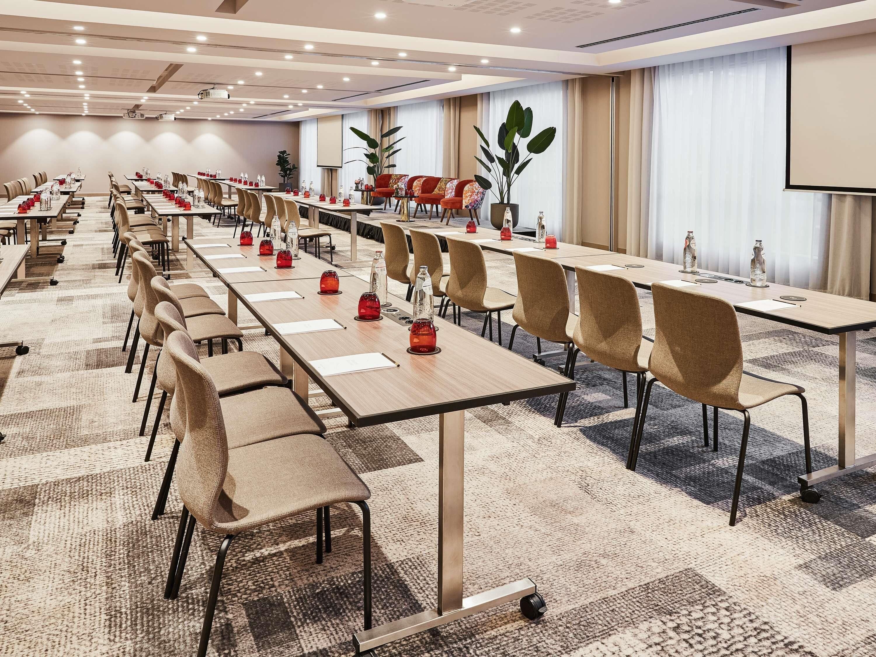 A conference room with long tables, chairs, and a projector screen.