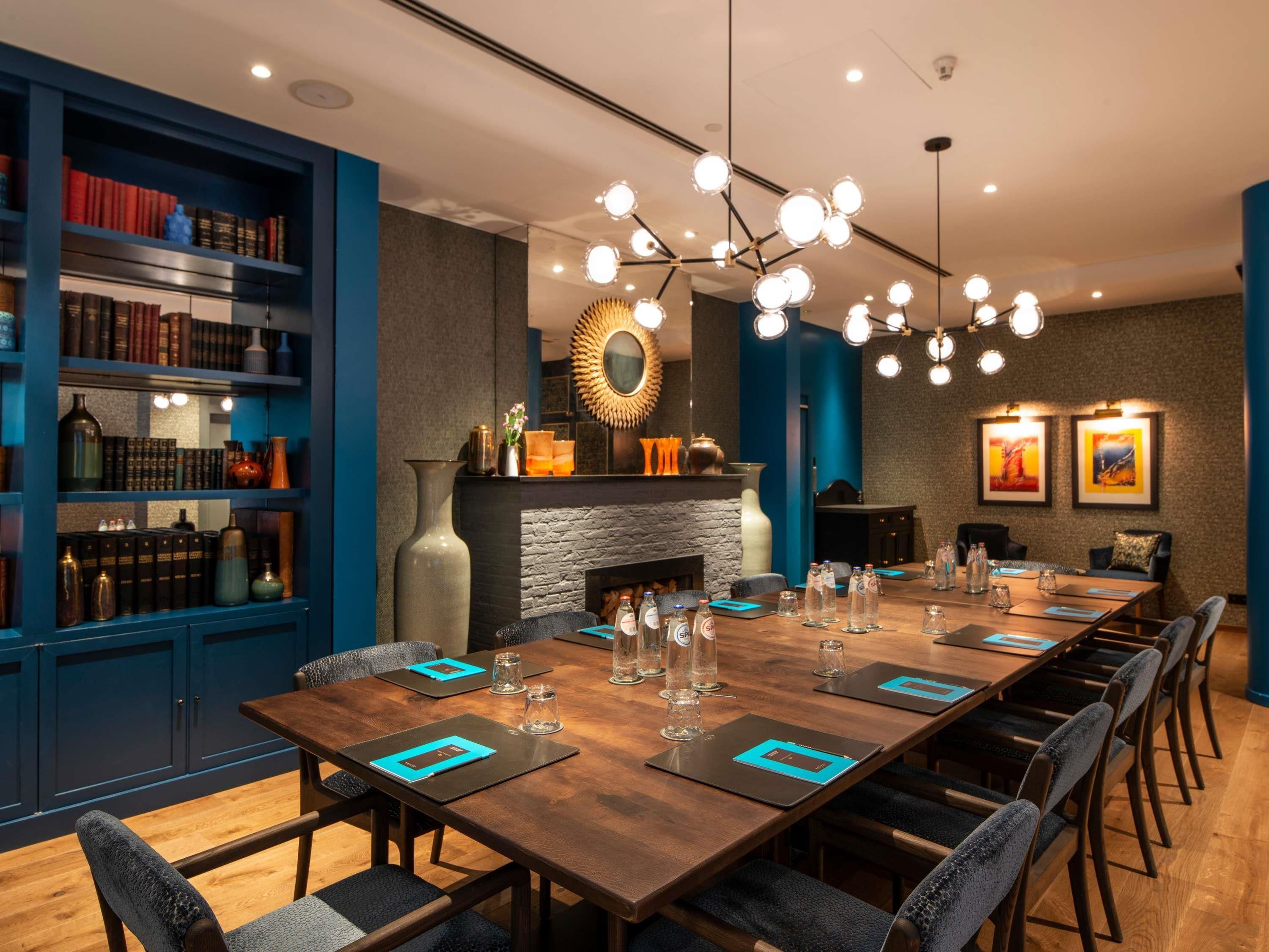 A conference room with a long table, chairs, a fireplace, bookshelves, and a modern chandelier.