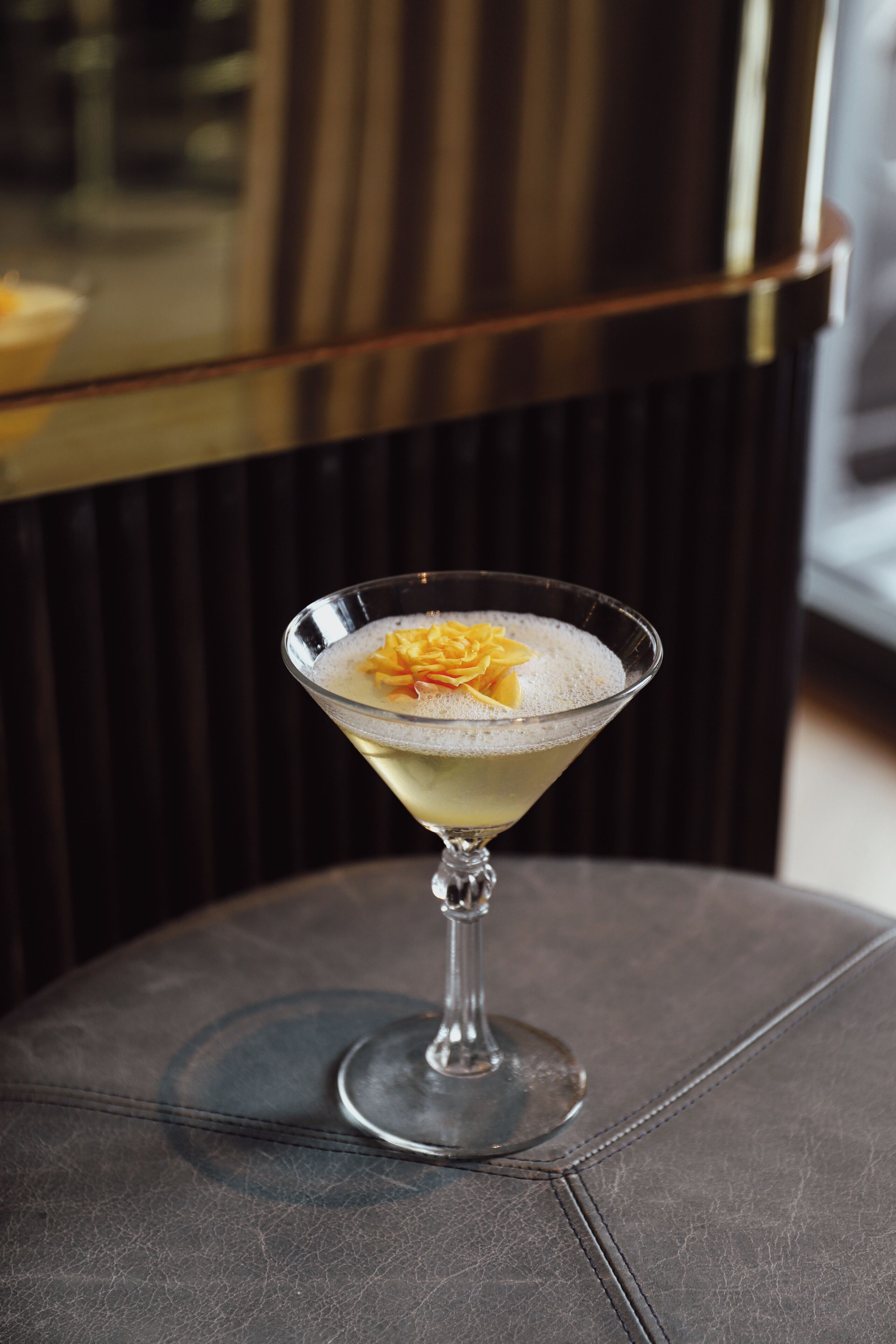 Un cocktail servi dans un verre à martini, agrémenté d’une décoration, posé sur un fauteuil en cuir foncé.