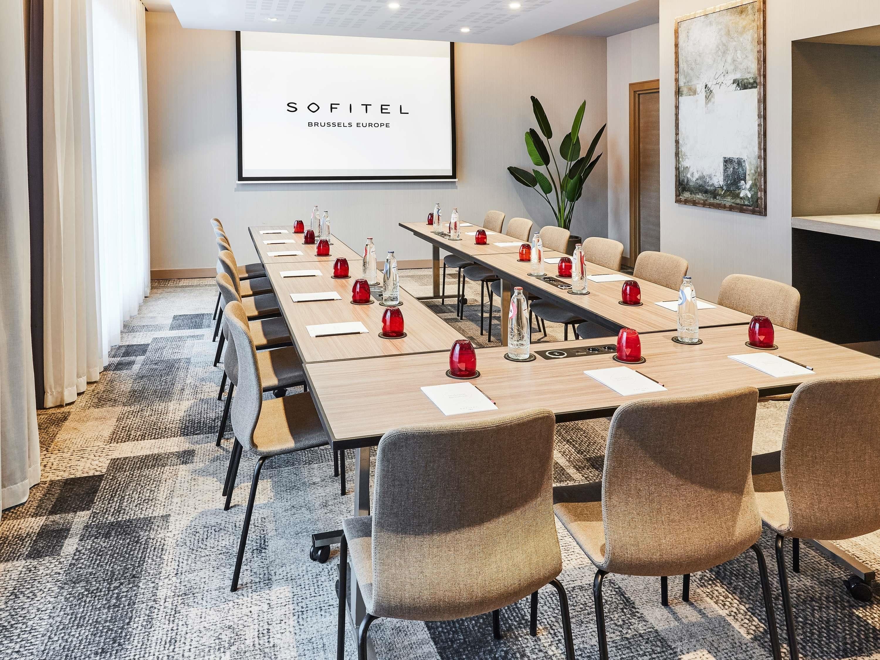 Un salón de conferencias con una larga mesa, sillas y una pantalla proyectora mostrando 'SOFITEL BRUSSELS EUROPE'.