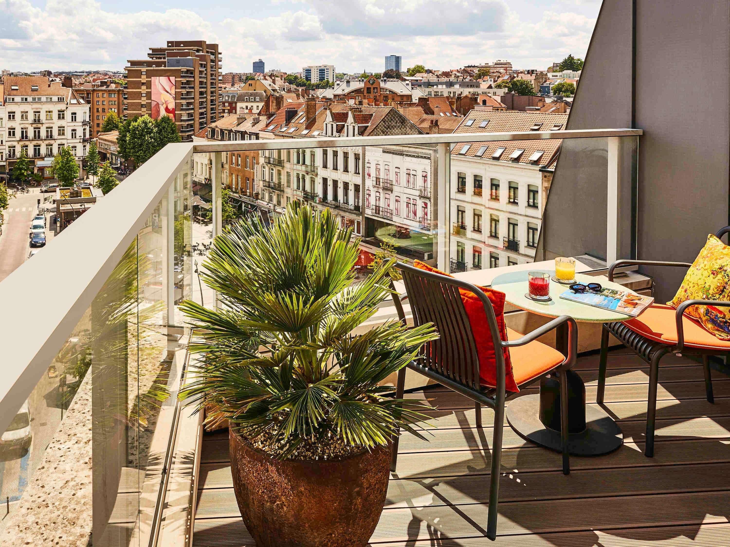 En balkon med et bord, stole, en potteplante og udsigt over bybilledet.