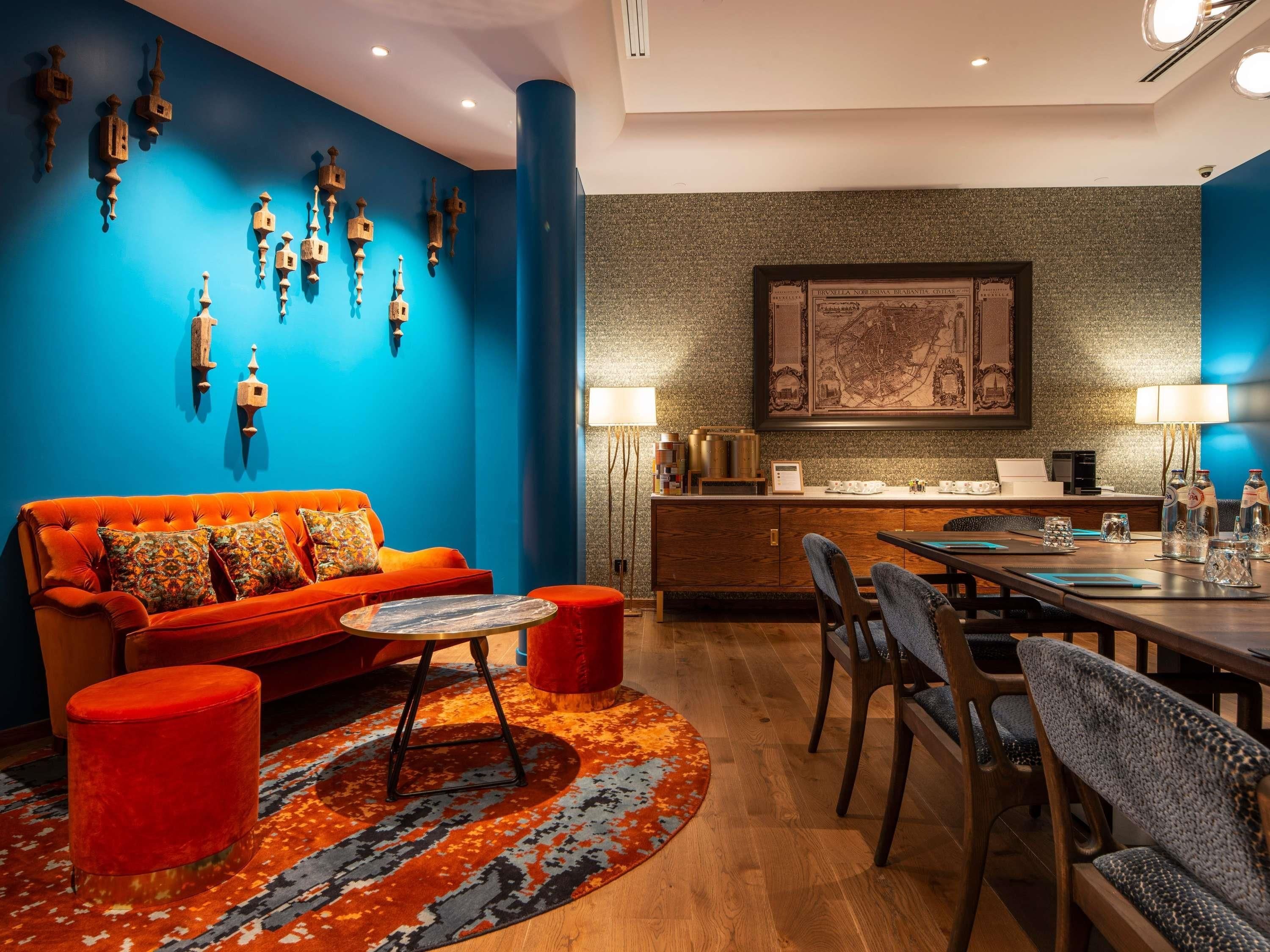 Una habitación de hotel moderna con una pared de acento azul, un sofá, una mesa de comedor y una zona de café.