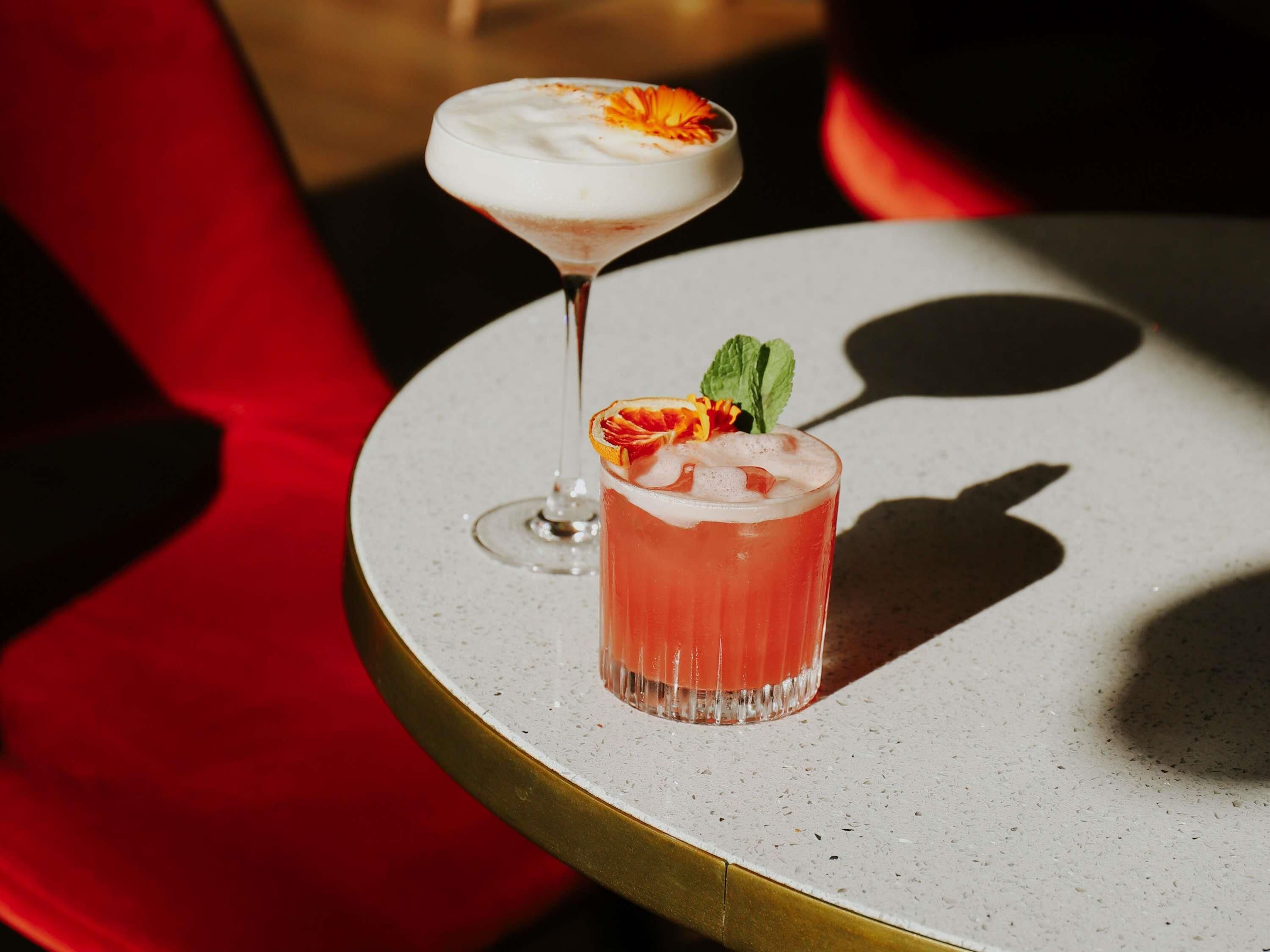 A round table with two drinks, one in a martini glass and one in a short glass, with a red chair in the background.