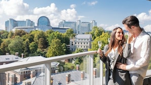 A couple on a balcony with a cityscape view, including modern buildings and greenery. - Sofitel Brussels Europe (Brussels)