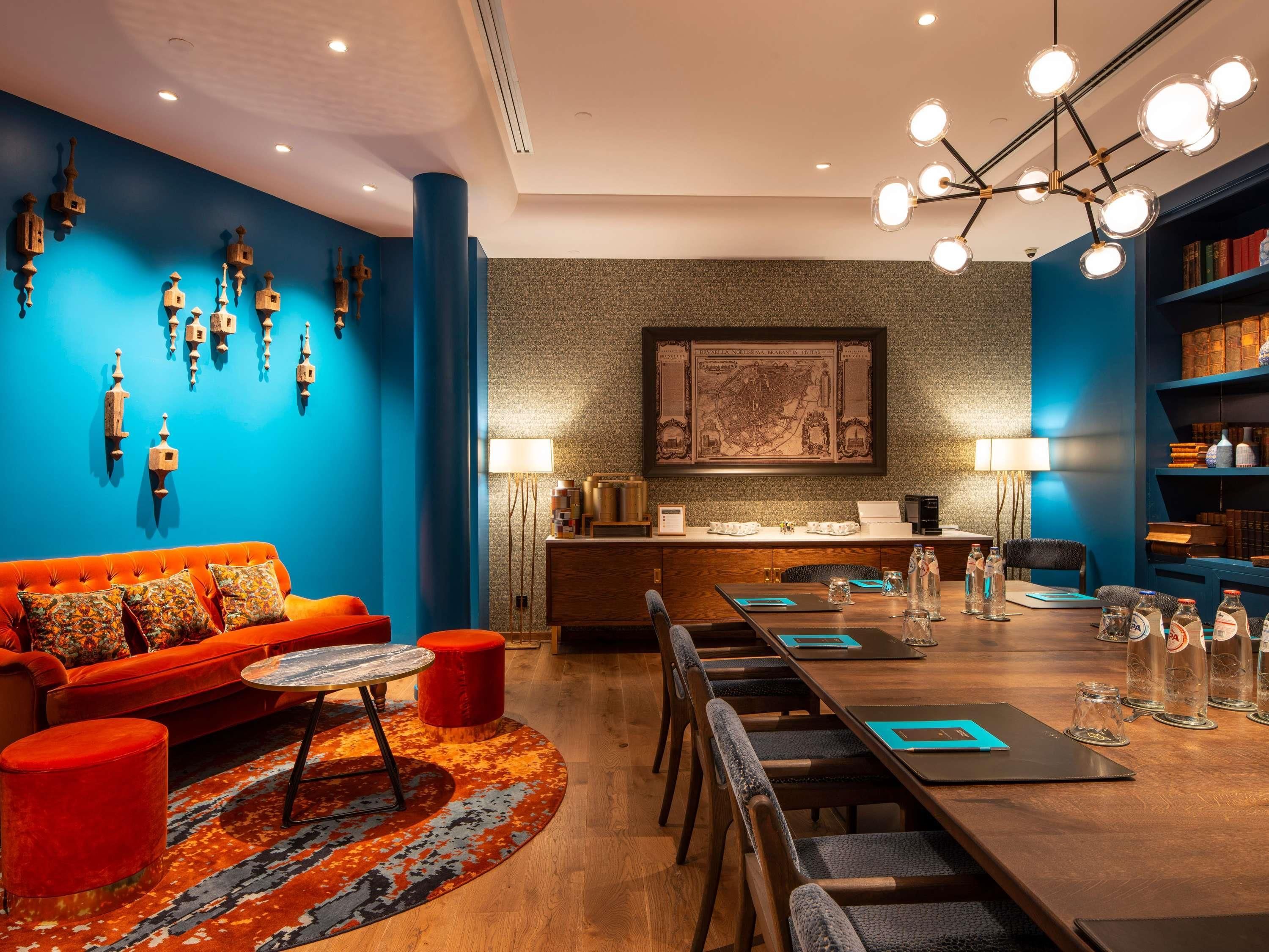 Une chambre d’hôtel moderne avec un mur d’accent bleu, un canapé rouge, une table à manger en bois et une bibliothèque.