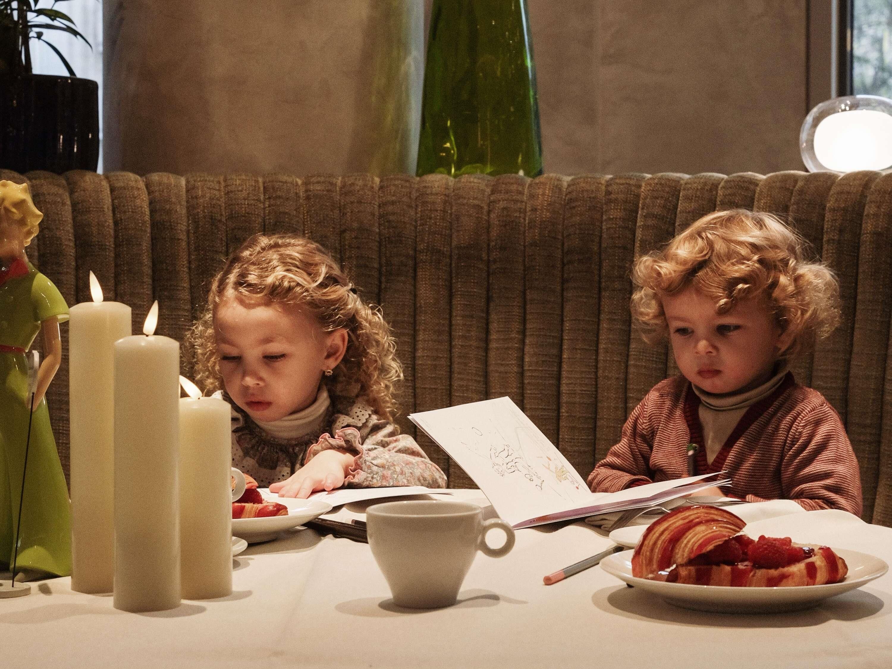 Dos niños sentados a una mesa con velas, un plato de comida y un libro.