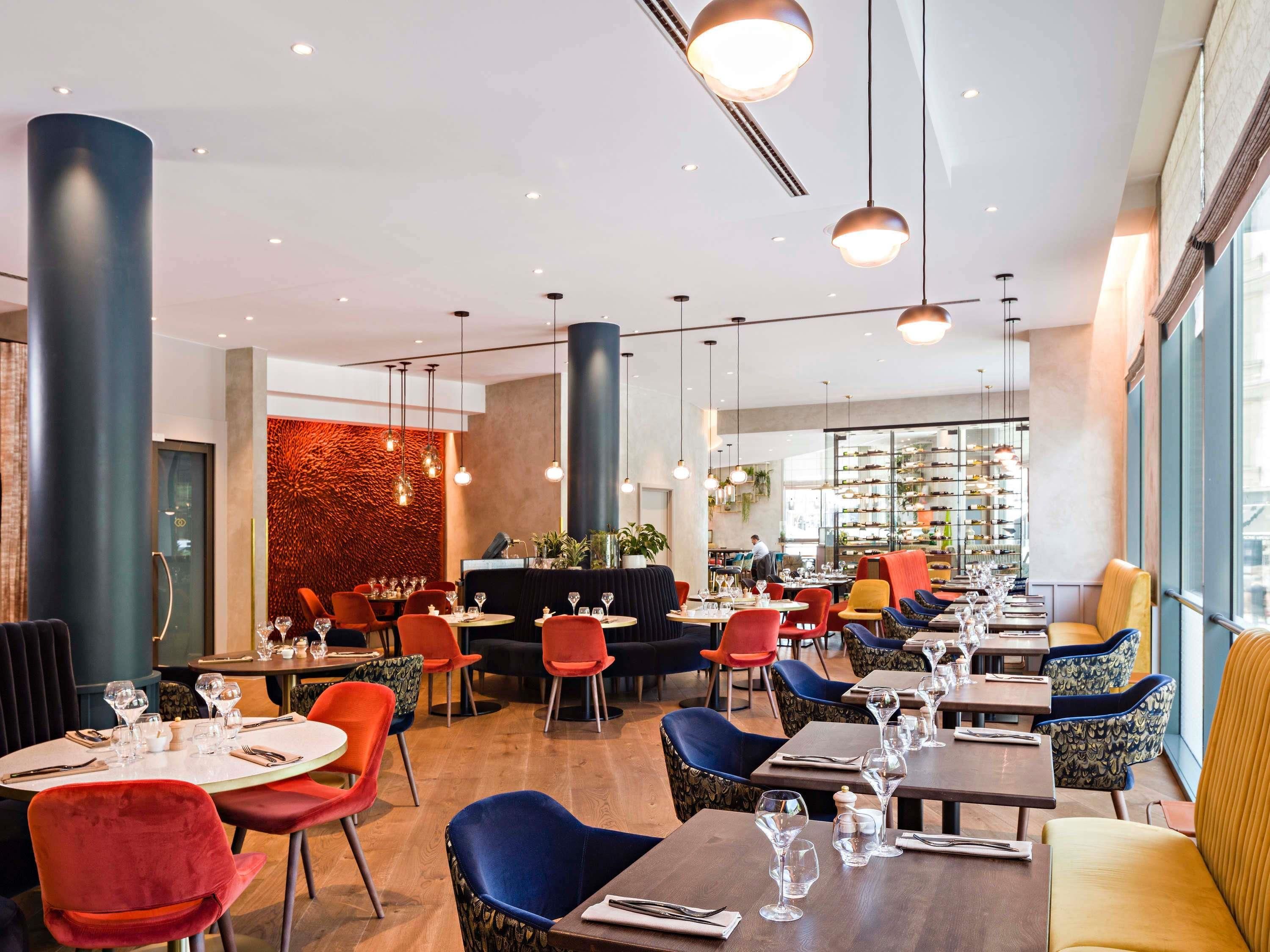A restaurant interior with round tables, chairs, and hanging pendant lights.