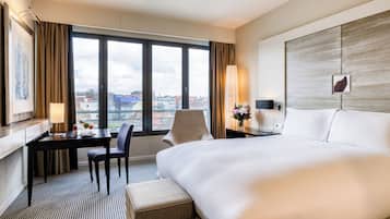Habitación de hotel con una cama grande, un escritorio con una silla, una lámpara y vistas de la ciudad a través de la ventana.