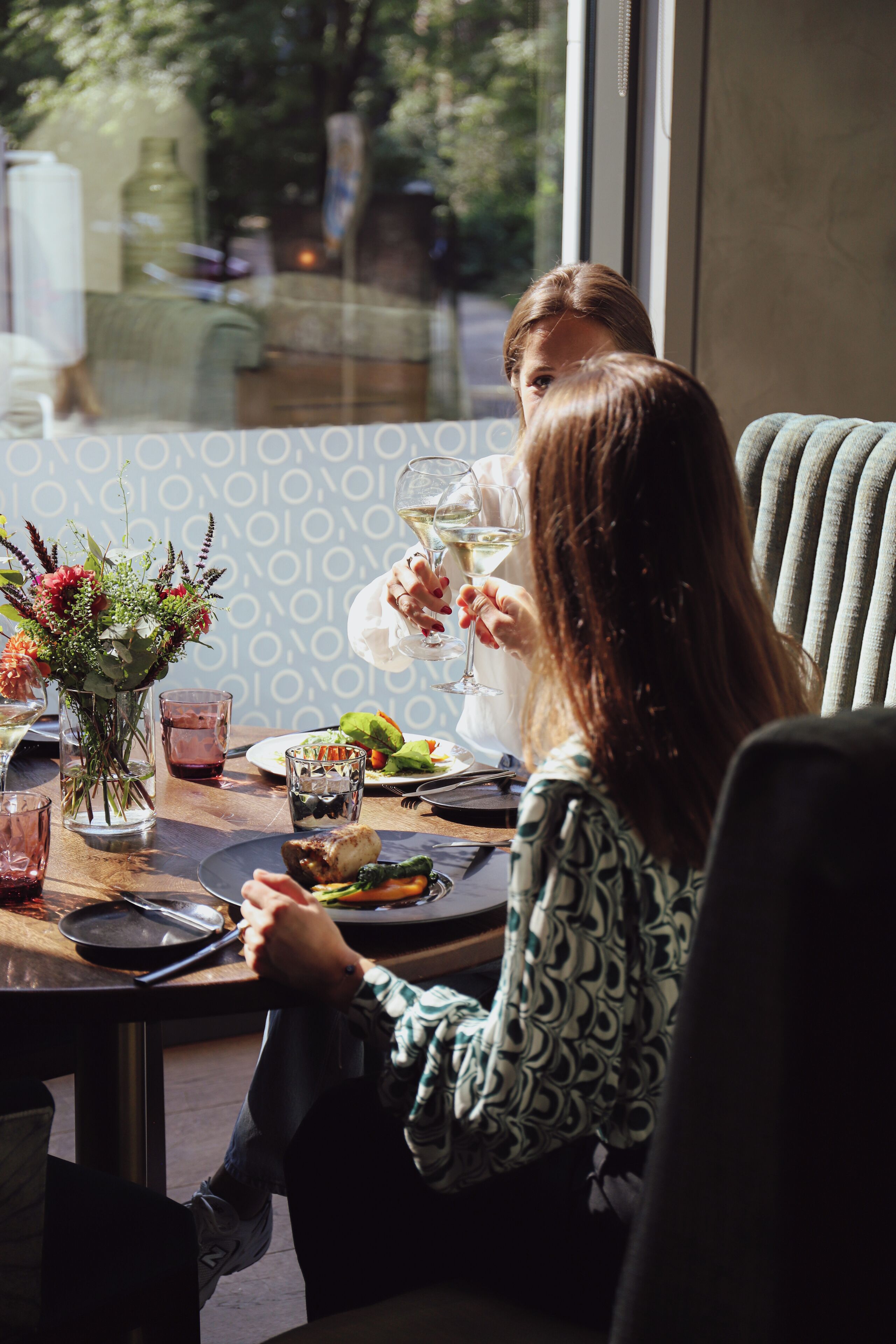 A dining table with a vase of flowers, a glass of wine, and a plate of food.