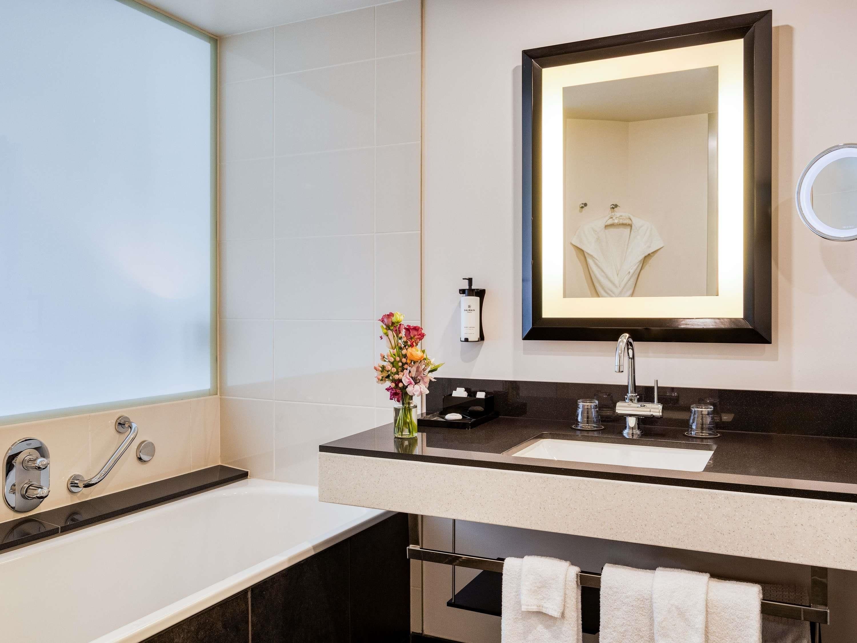 A modern bathroom with a large mirror, a bathtub, a vanity with a sink, and a towel rack.