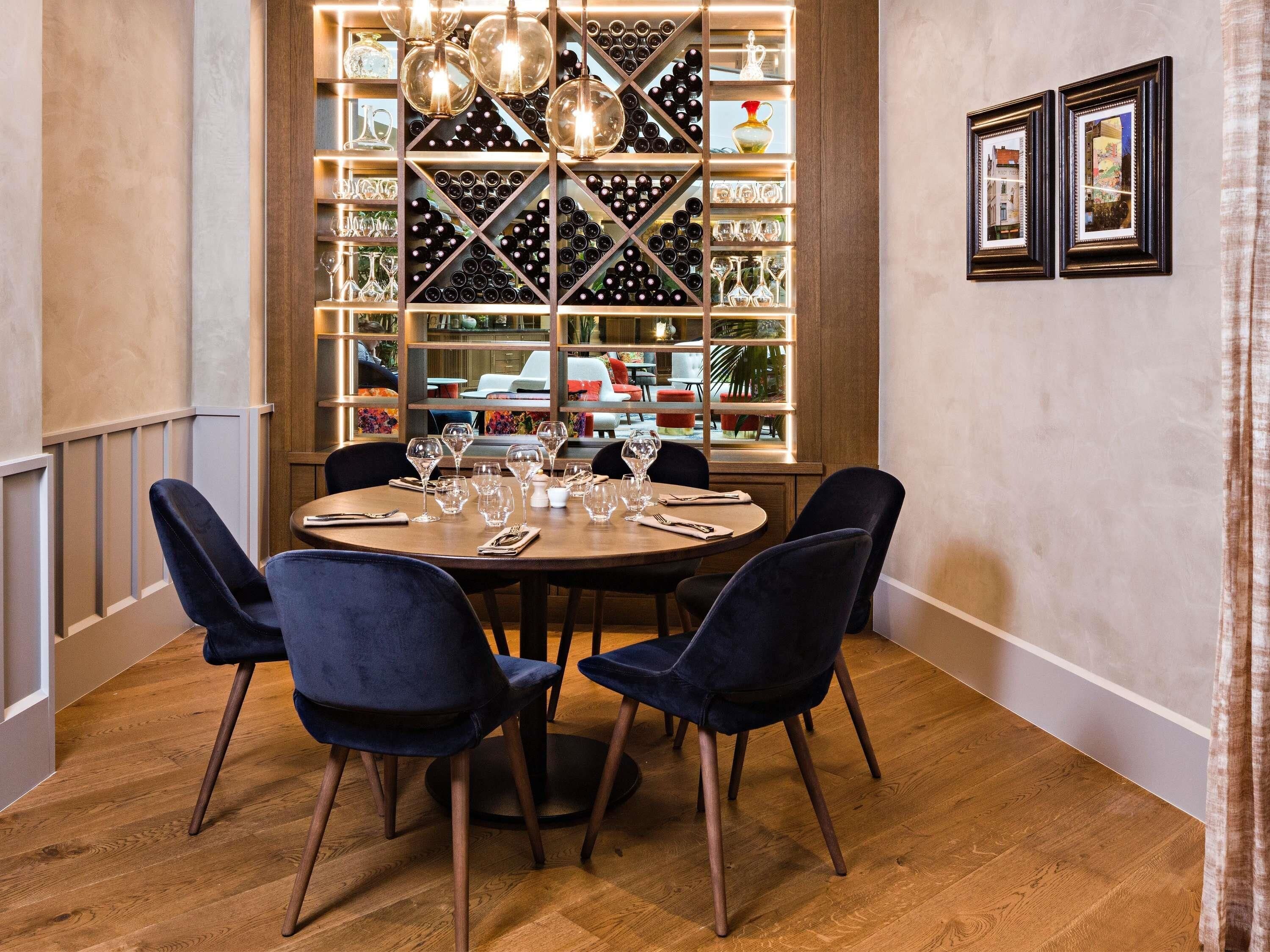Een eethoek met een ronde tafel, vier stoelen en een wijnrek met flessen en glazen achter een raam.
