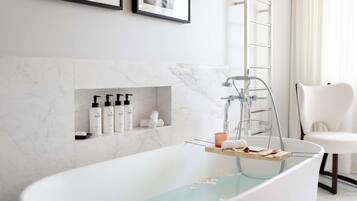 Un baño moderno con una bañera independiente, paredes de mármol, un perchero y un estante con artículos de aseo.