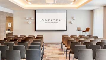 Une salle de conférence avec des rangées de chaises, un écran de projection et un panneau encadré.
