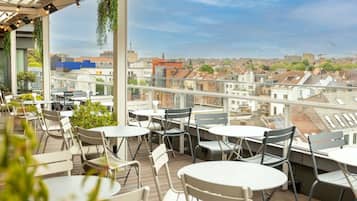 Una terraza en la azotea con mesas y sillas, con vistas a un paisaje urbano.
