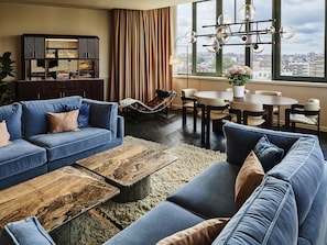 Una sala moderna con un conjunto de sofás, una mesa de centro, una mesa de comedor con sillas, un sillón colgante y vistas de la ciudad a través de amplias ventanas.