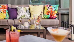 A modern living room with a sofa adorned with colorful pillows, a glass table with drinks, and a view of the outdoors. - Sofitel Brussels Europe (Brussels)