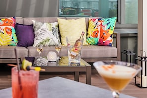 A modern living room with a sofa adorned with colorful pillows, a glass table with drinks, and a view of the outdoors. - Sofitel Brussels Europe (Brussels)
