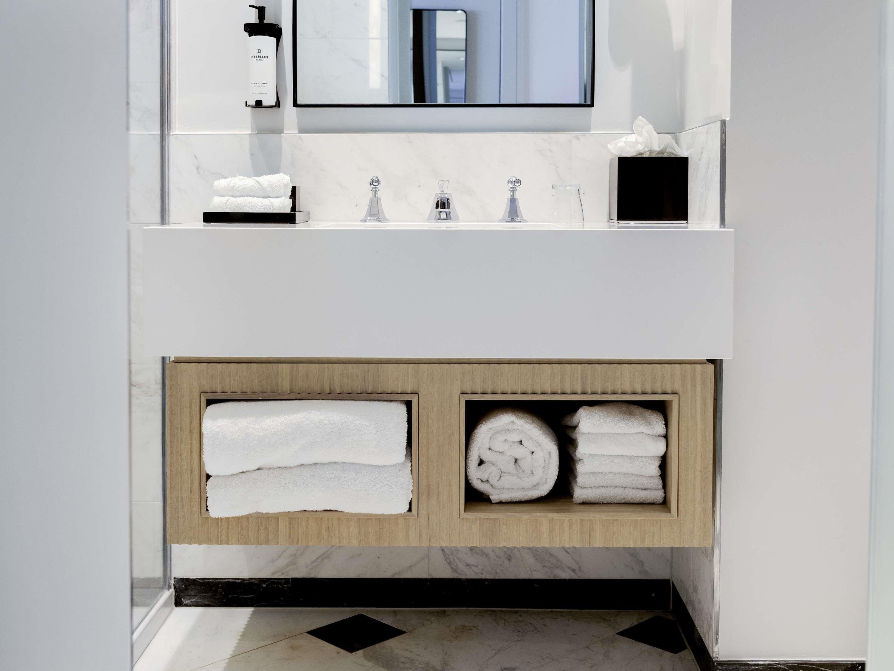 A modern bathroom with a white vanity, a mirror, a towel rack, and a shelf with neatly folded towels.