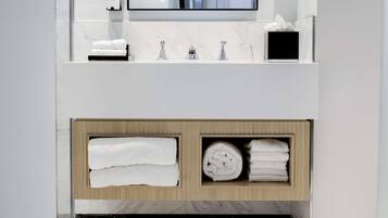 A modern bathroom with a white vanity, a mirror, a towel rack, and a shelf with neatly folded towels.