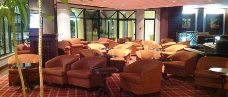 A lobby with orange armchairs, a checkered floor, and a large potted plant.