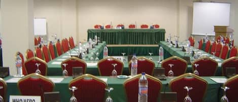 A conference room with rows of red chairs, green tables, nameplates, and a podium.
