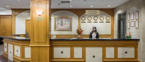 Un comptoir d’accueil avec un panneau « Il est interdit de fumer », un tableau représentant une zèbre encadré, des horloges et des certificats encadrés accrochés au mur.