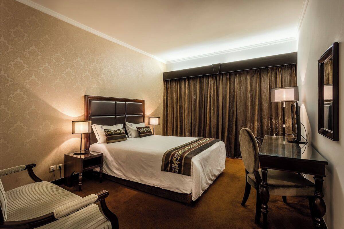 A hotel room with a bed, bedside table, lamp, chair, desk, and a mirror.
