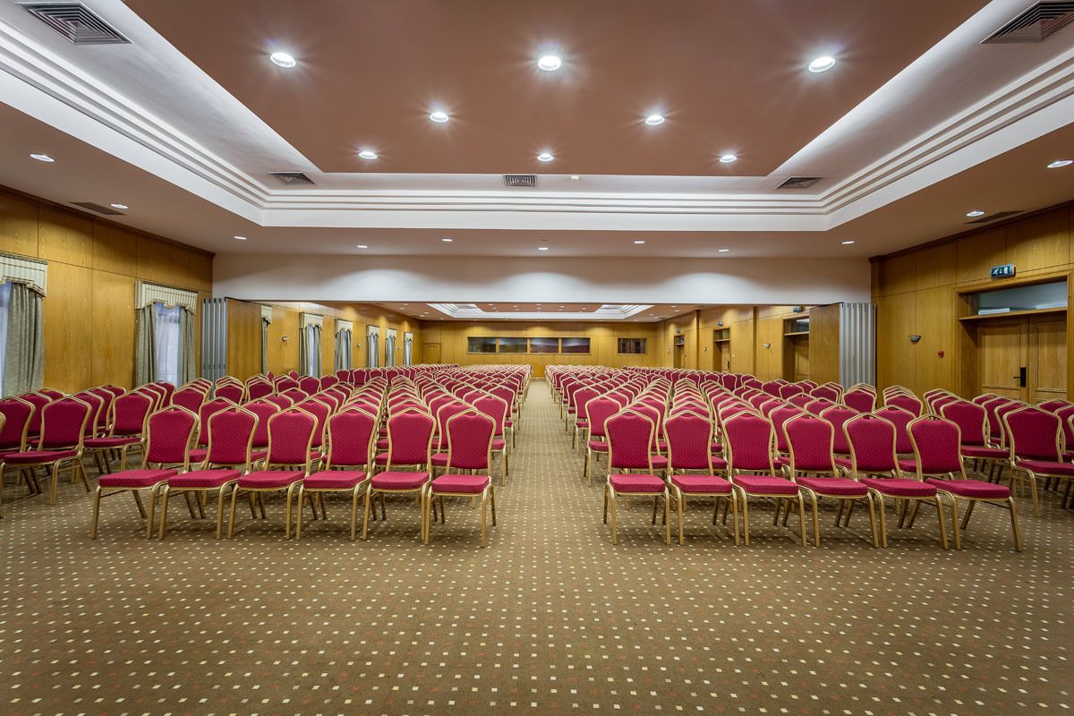 Un salón de conferencias con filas de sillas rojas y piso alfombrado.
