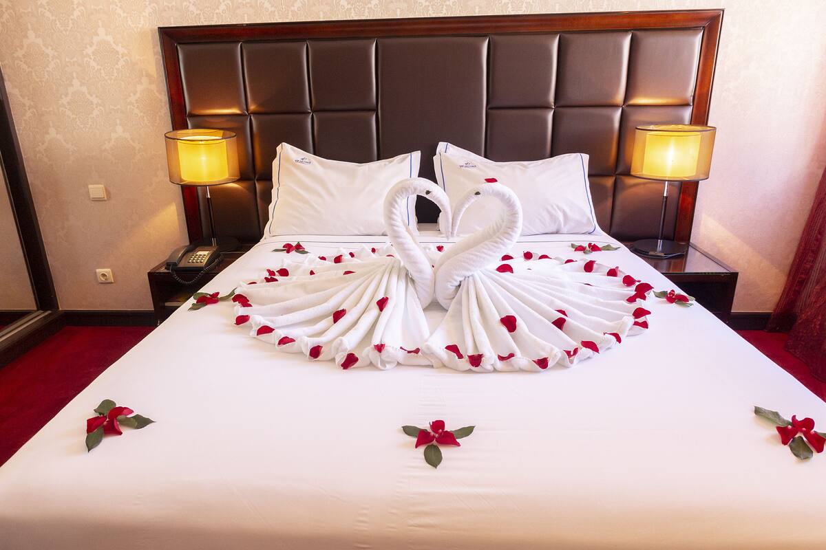 A hotel room with a neatly made bed, two bedside lamps, and a telephone on the nightstand.