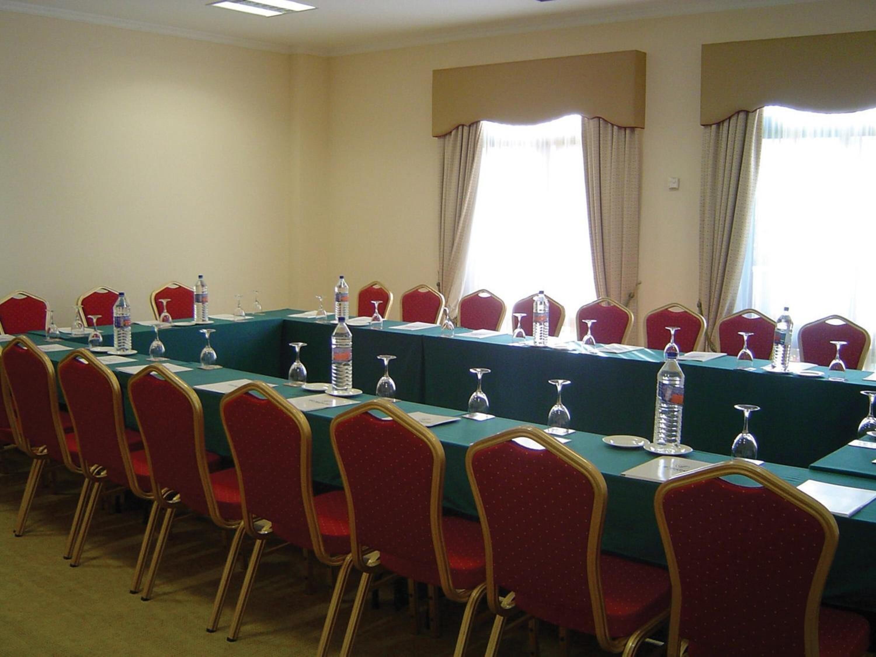 A conference room with a long table, red chairs, water bottles, and wine glasses.