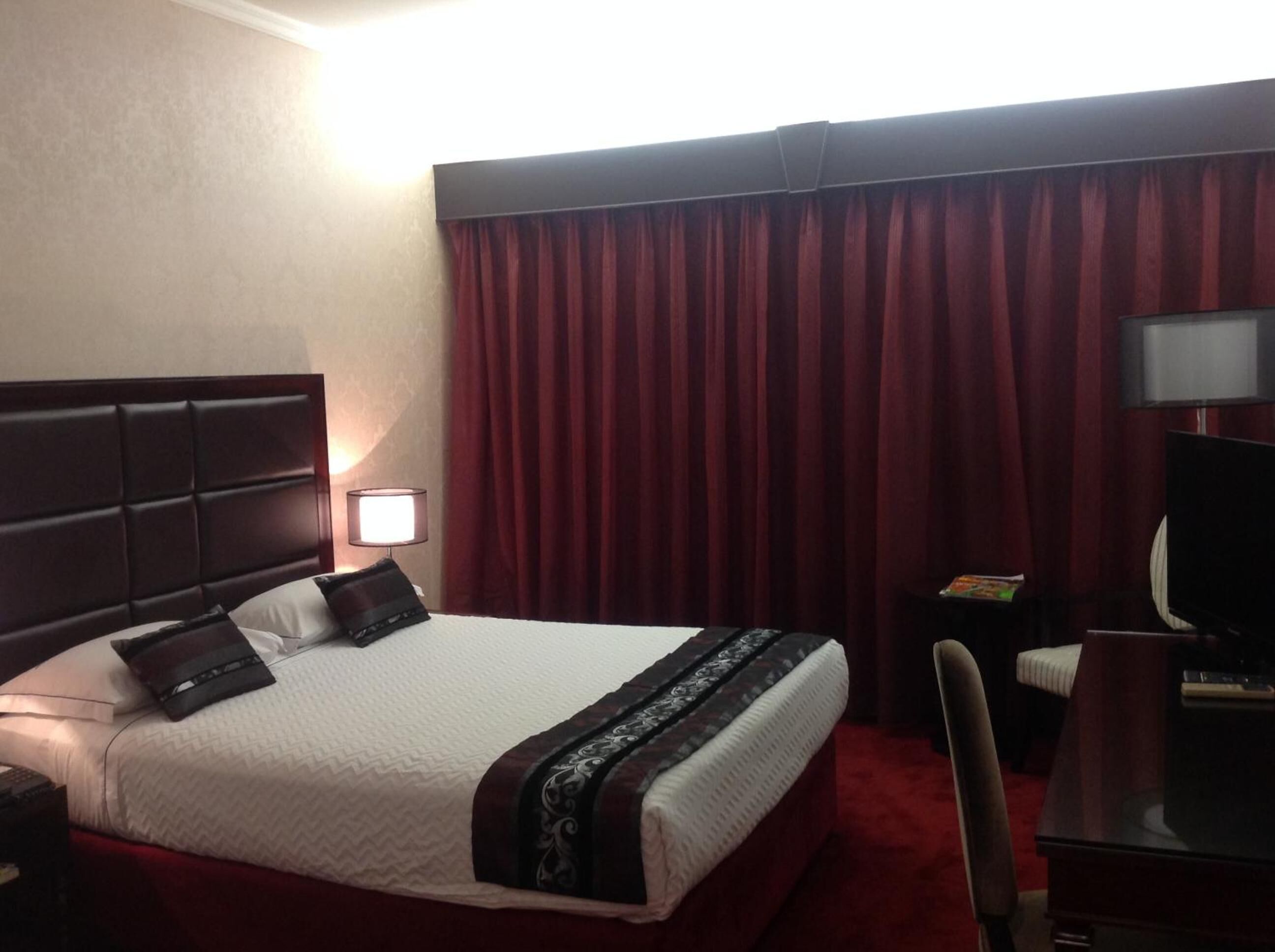 A hotel room with a large bed, a desk with a chair, a TV, and a lamp.