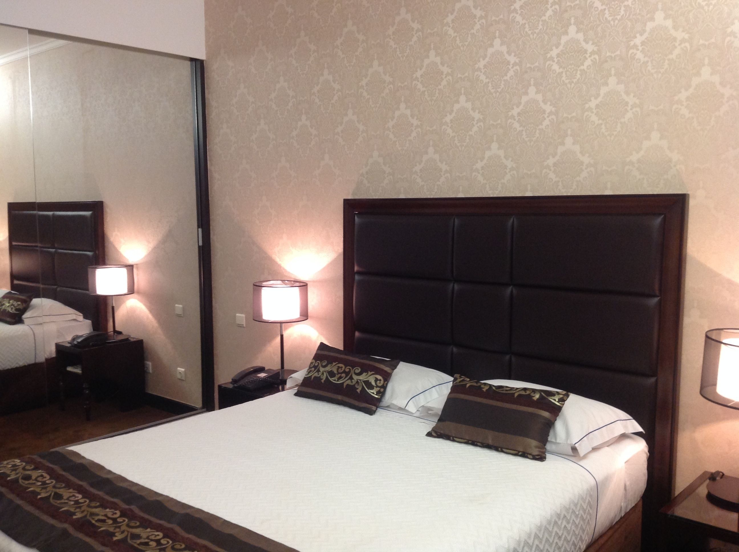 Habitación de hotel con una cama grande, dos mesitas de noche, un espejo y un papel tapiz estampado.